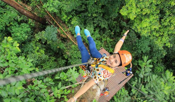 Woman enjoying a thrilling zipline experience in Phuket, Thailand's vibrant green forest.